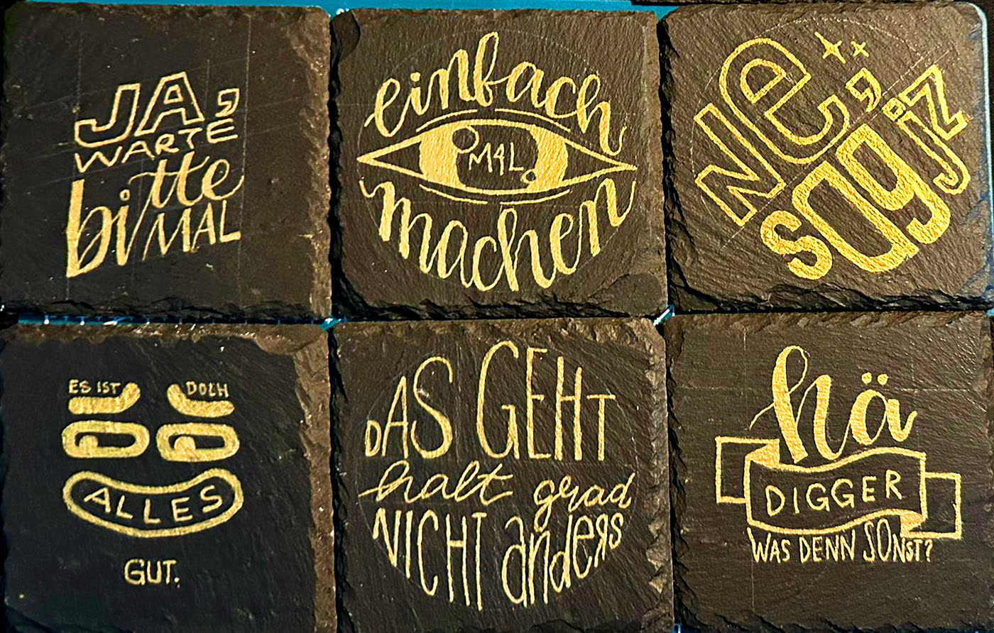 Sechs handgeletterte Sprüche in Gold auf Schiefertafeln