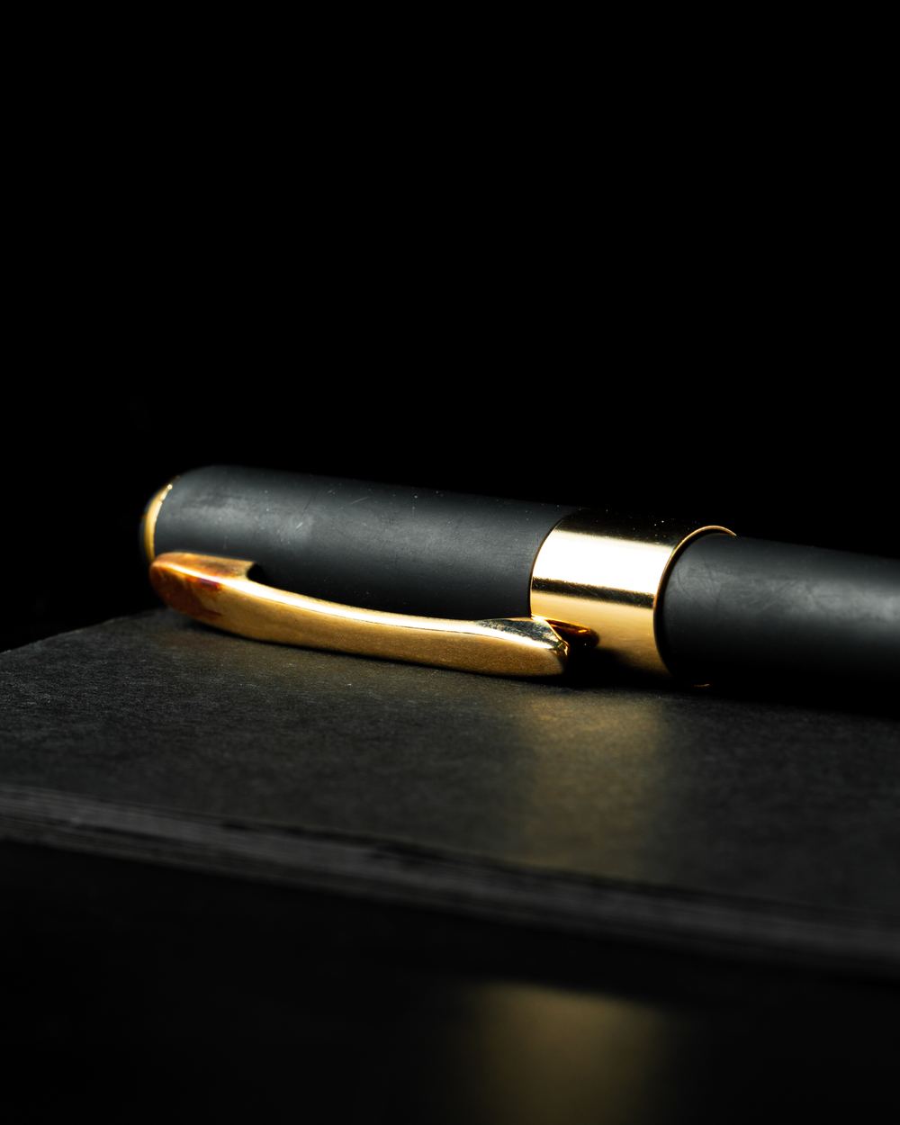 Stimmungsbild: schwarzer Stift mit Gold-Clip auf schwarzem Notizblock