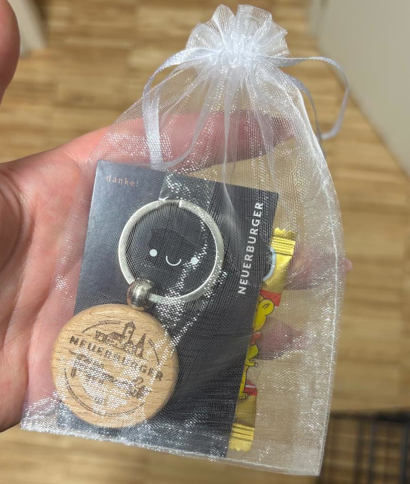 Holz-Schlüsselanhänger mit Logo auf schwarzer danke-Karte, mit Gummibärchen in einem weißen Organzasäckchen